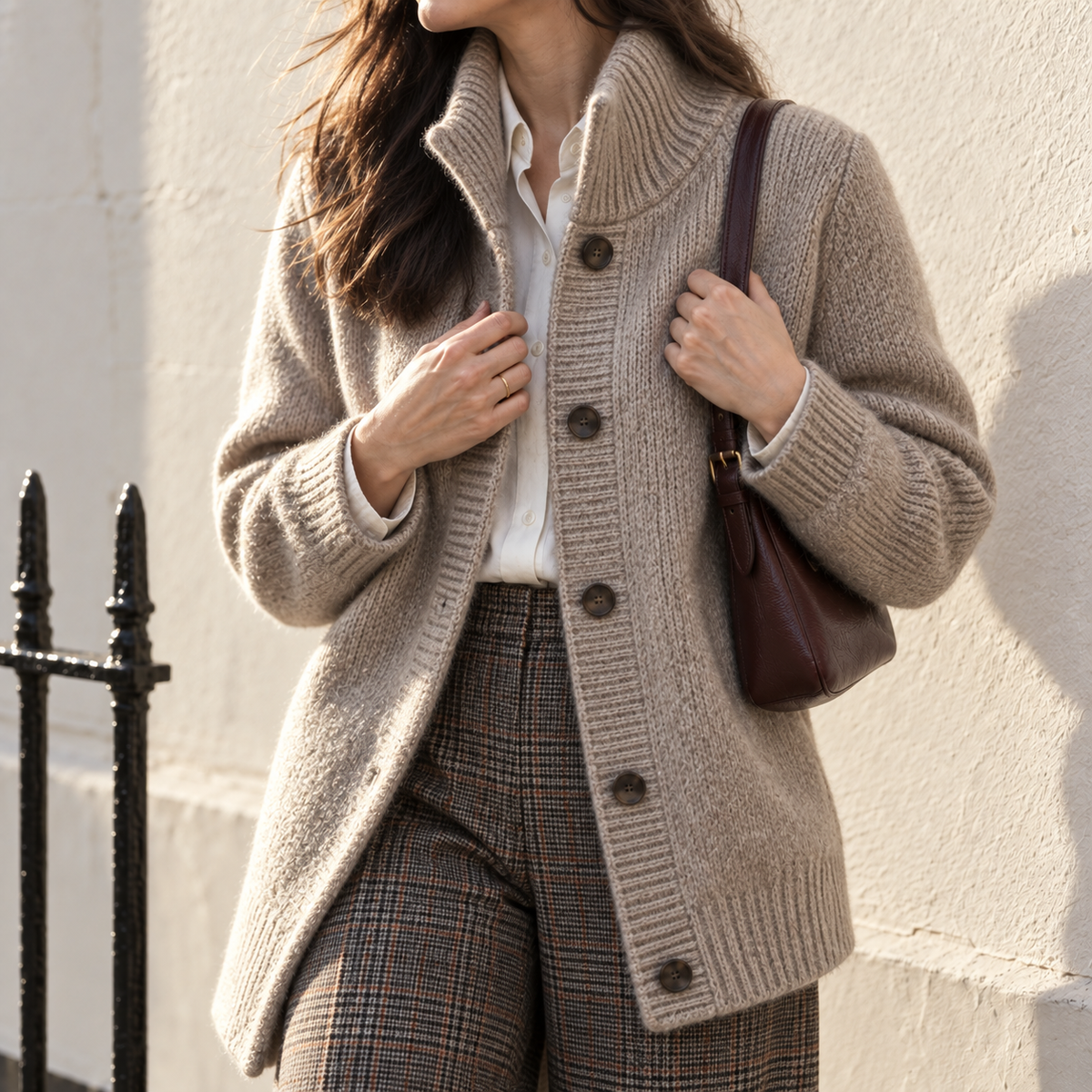 Close view of an oatmeal wool cardigan, cream shirt and brown check trousers